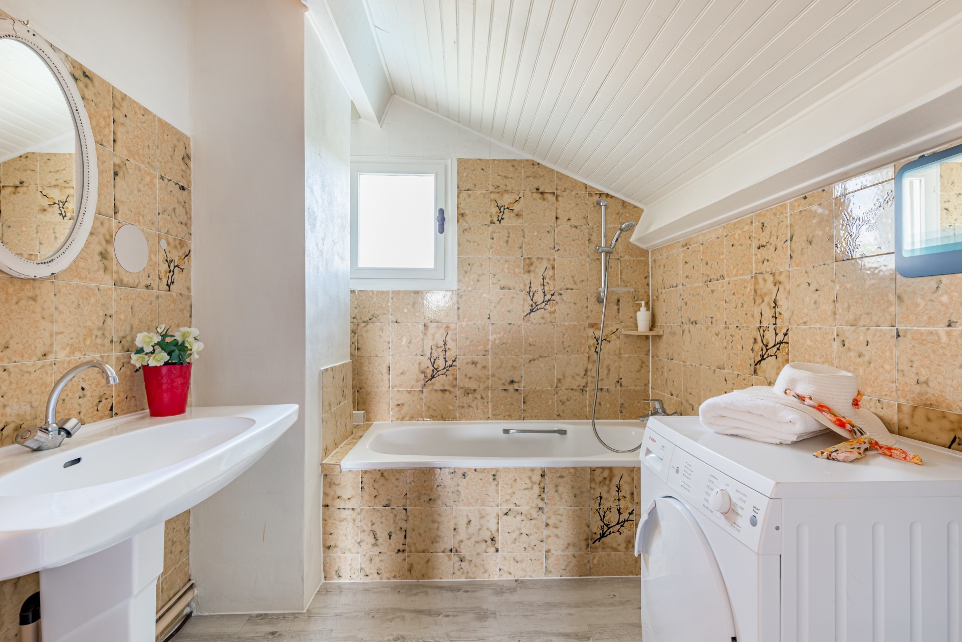 Salle de bain de la suite Perle : baignoire, vasque, chapeau posé sur le sèche-linge et plafond blanc