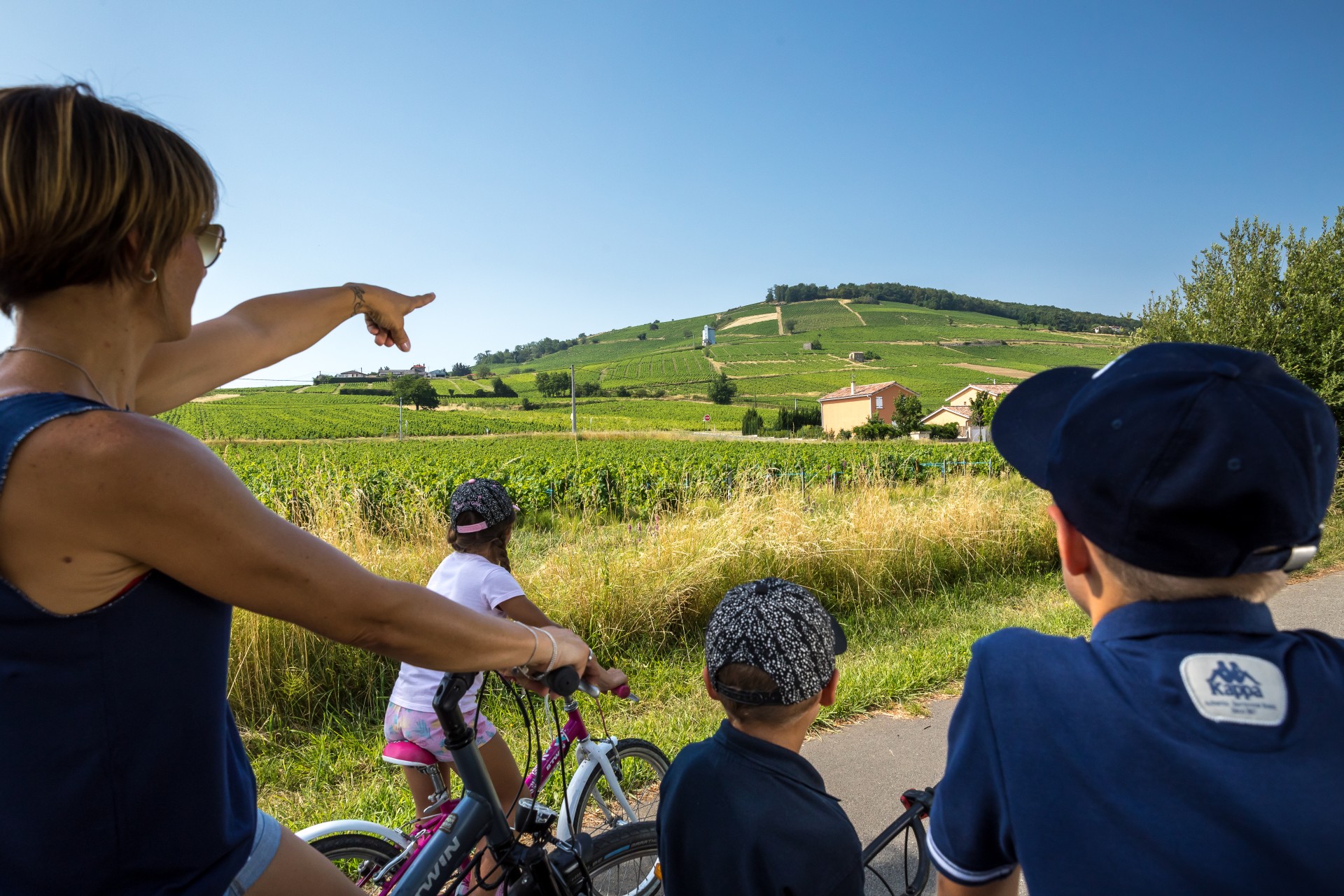 Una madre e i suoi tre figli stanno pedalando in estate. Si sono fermati di fronte al Mont Brouilly, ricoperto di vigneti nella regione del Beaujolais.