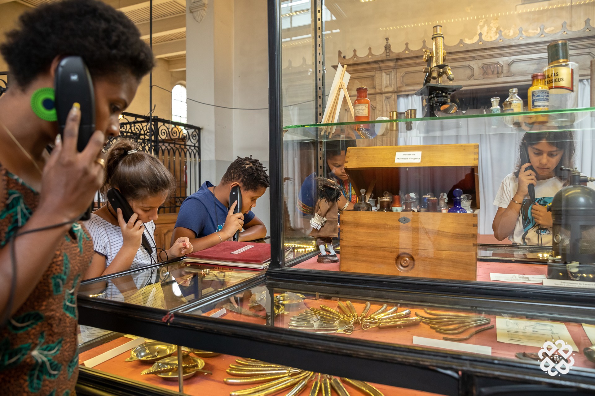 Une famille avec une mère et ses enfants qui sont en train d'écouter des informations historiques avec un audioguide et en même temps elles regardent des objets anciens, dans une salle du musée de l'hôtel dieu à Belleville.