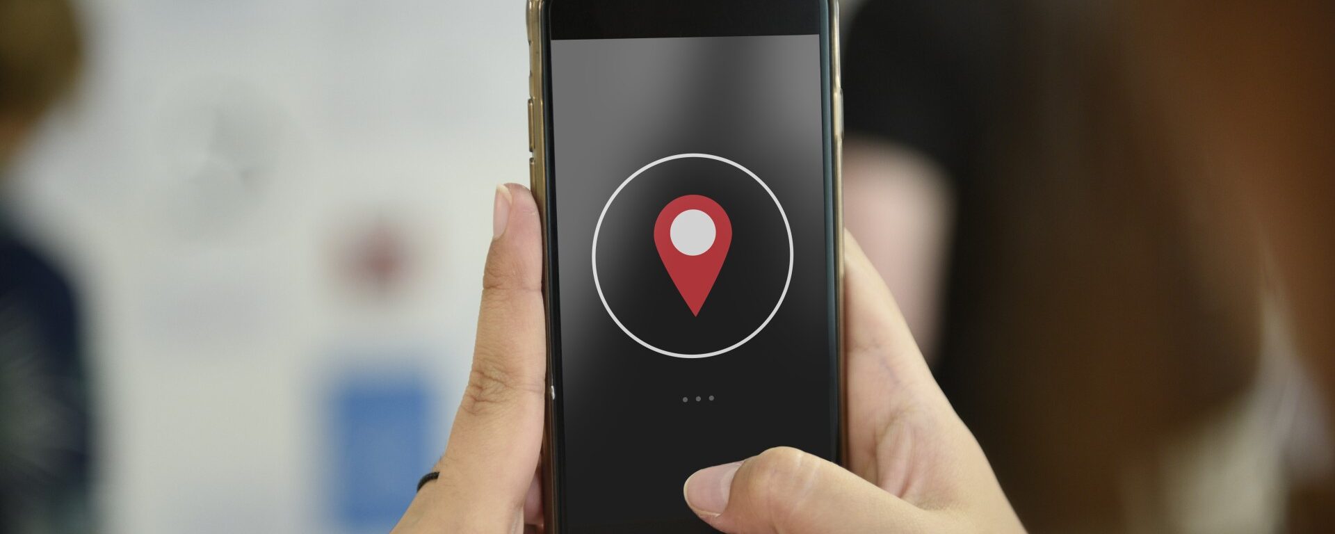 Des mains qui tiennent un portable avec un point de geolocalisation rouge au centre du portable.