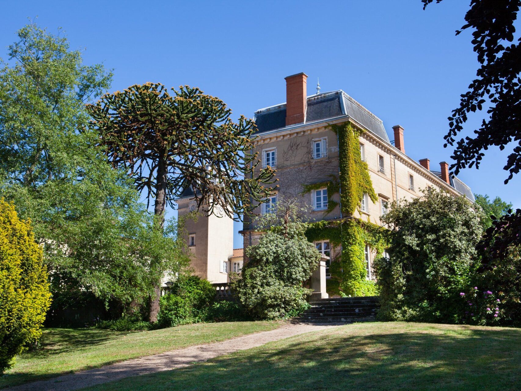 Une partie du château de Bellevue prise depuis le parc arboré. Une montée d'escaliers en pierre mène à l'édifice. Villié-Morgon, Beaujolais