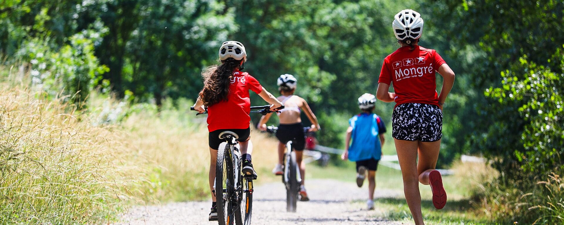 Personnes faisant une activité sportive à Villefranche-sur-Saône, bordelan. Deux enfants sont à vélo et deux autres sont en train de courir sur un chemin en terre avec des arbres autour.