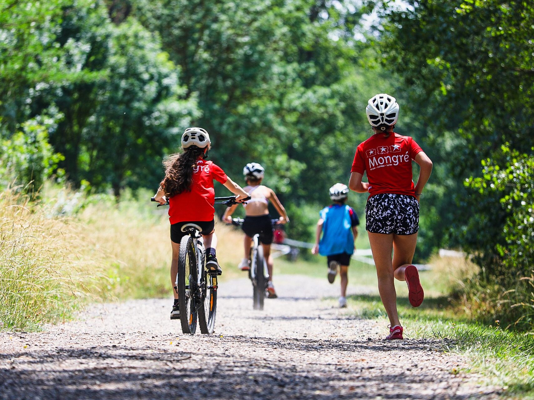 Personnes faisant une activité sportive à Villefranche-sur-Saône, bordelan. Deux enfants sont à vélo et deux autres sont en train de courir sur un chemin en terre avec des arbres autour.