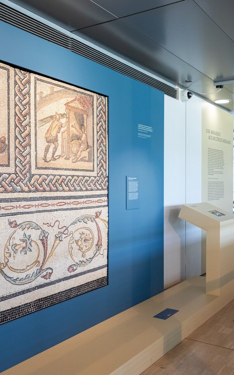 Ein Raum im Museum von Saint-Romain-en-Gal. Ein Mosaik und Informationen zur Ausstellung sind zu sehen. Ein Mann liest. 